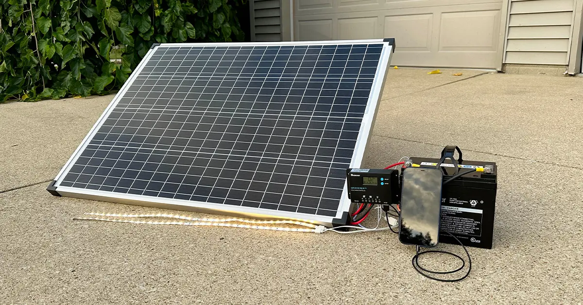 An image of a 100w solar panel hooked up to a charge controller and battery, powering LED lights and an iPhone.